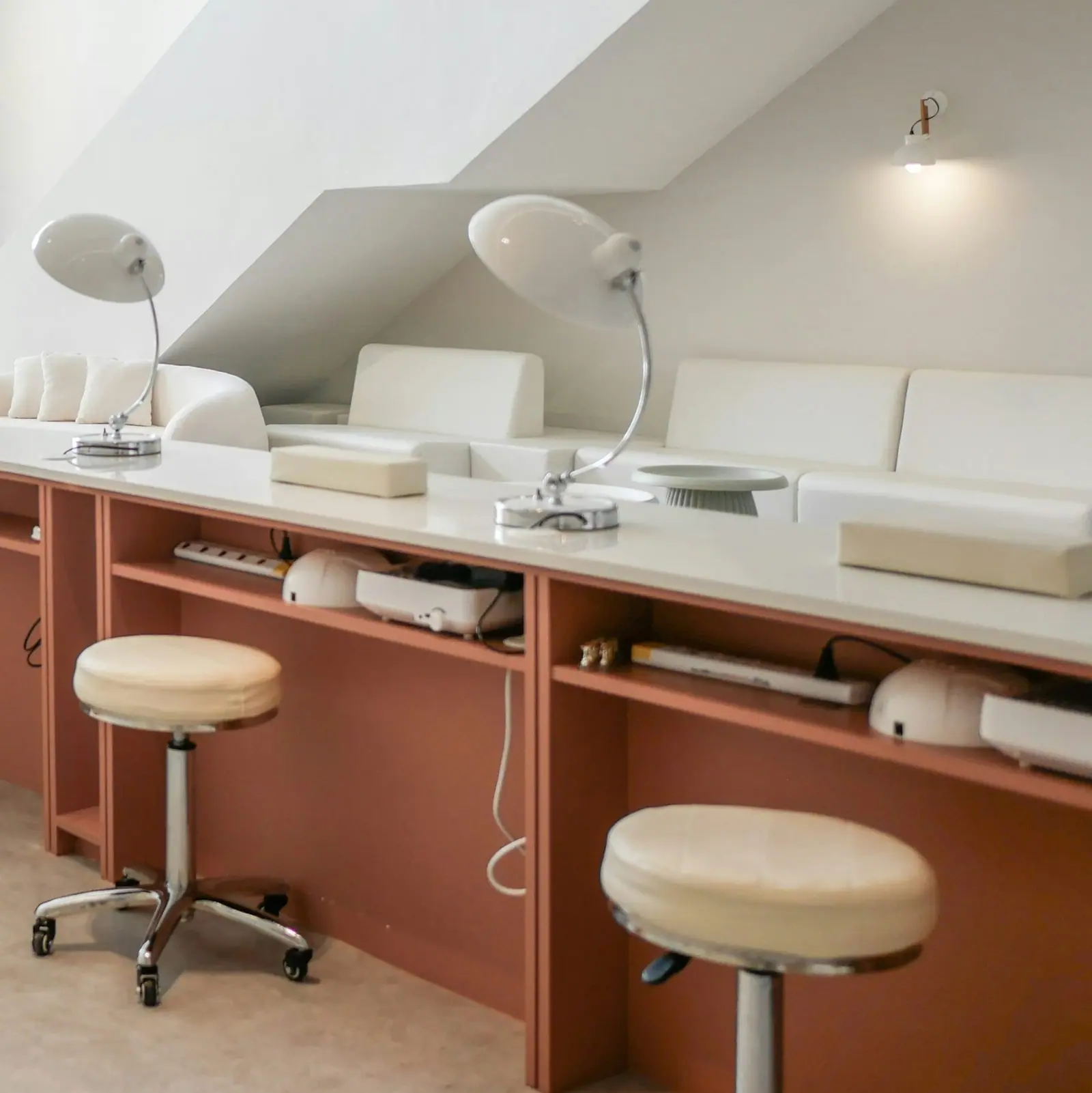 Dwa stanowiska manicure z lampami i taboretami pod skosem poddasza